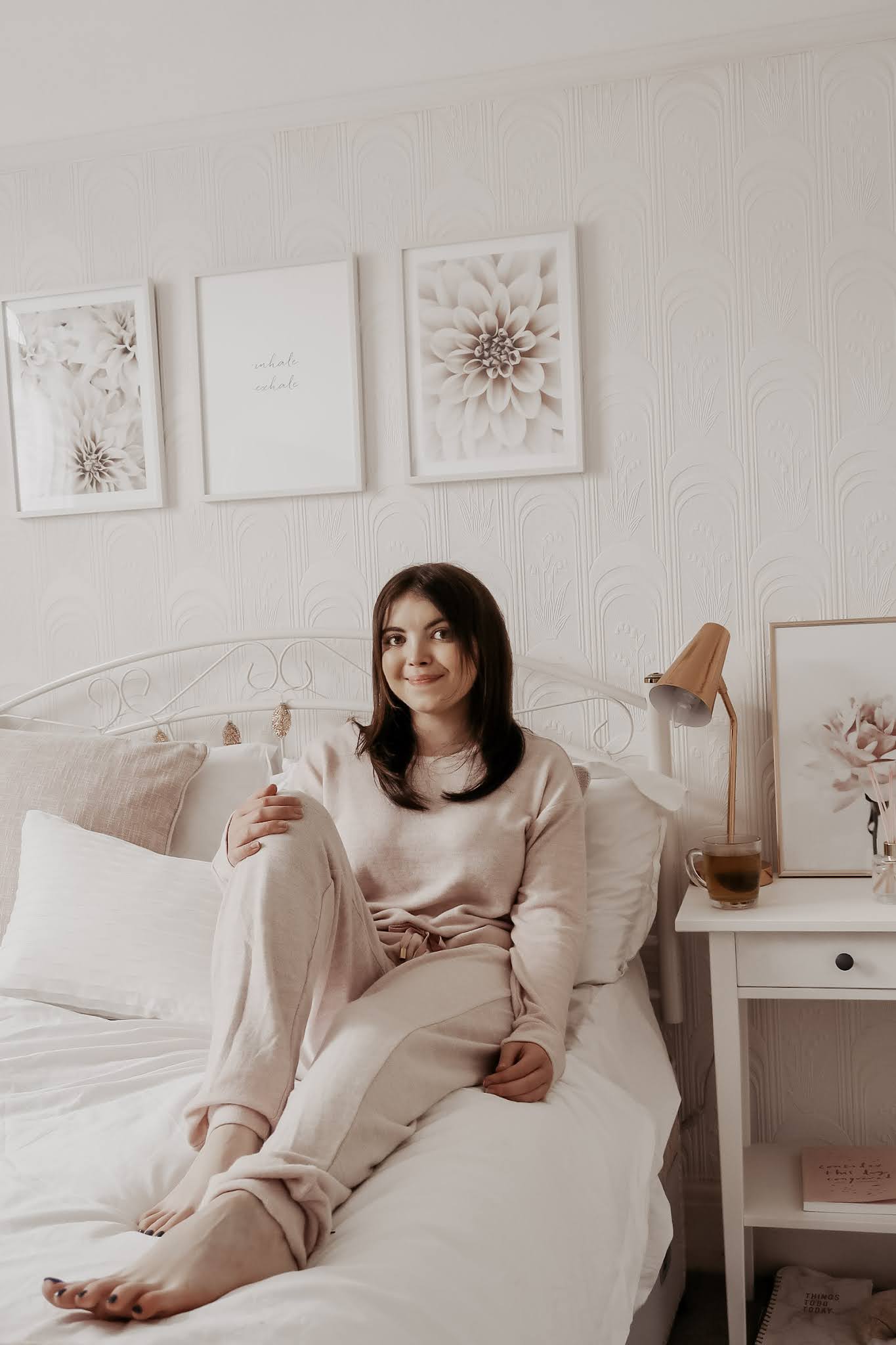 A woman sitting on a bed in a pink jumpsuit.