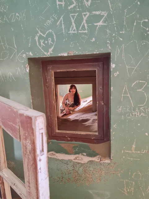 Girl looks through window in an abandoned home reclaimed by desert