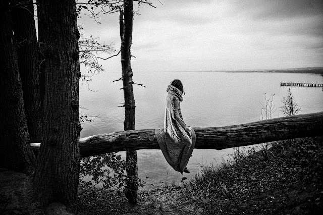 A woman siting on a dead tree, alone in the forest