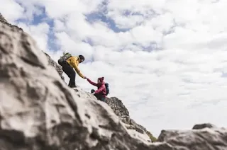 Two hikers helping one another up a rock