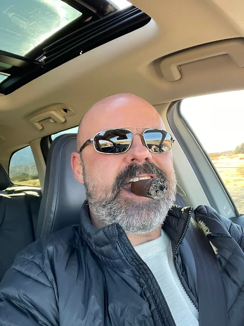Handsome bald man wearing a puffy shiny jacket smoking a cigar driving a car
