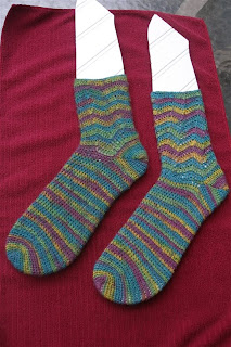  finished teal, green, yellow, and purple socks are shaped on sock blockers, which are laying on a maroon towel