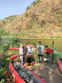 5 orang tersenyum berdiri di depan perahu kayak dengan background pemandangan sungai dan batuan kapur