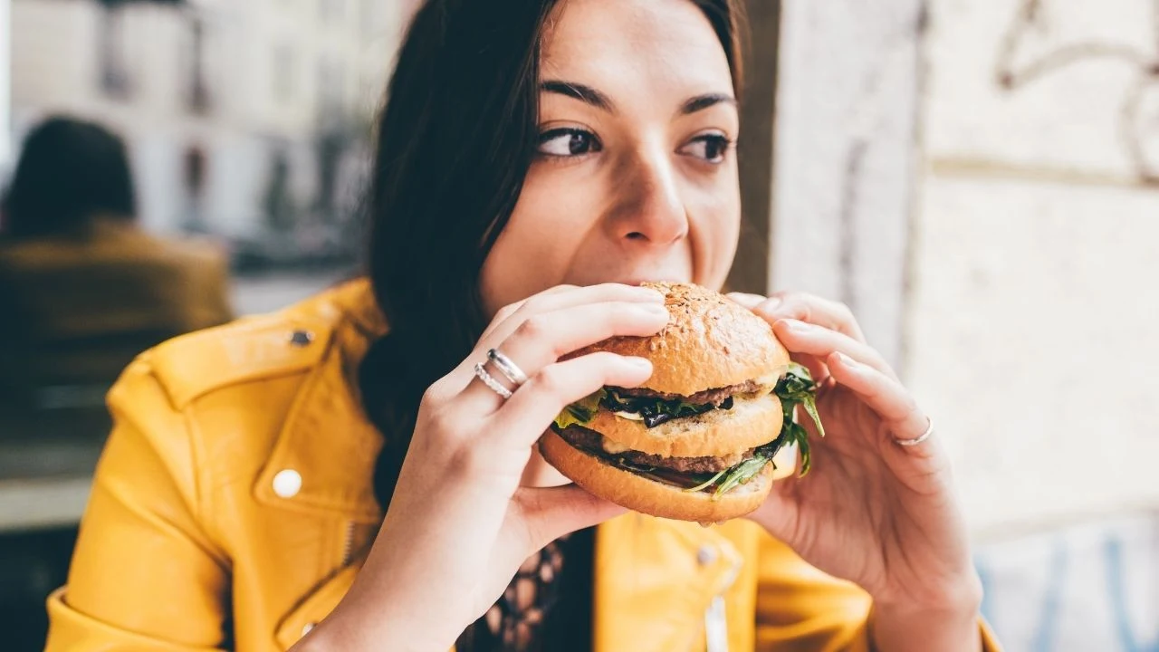 Young woman sitting in a restaurant eating an hamburger hand hold-hunger, food, meal concept.