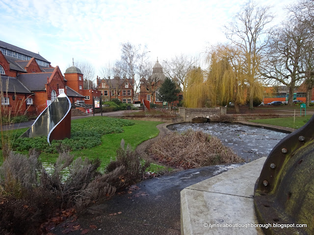 An icy pond in a park surrounded by red brick buildings