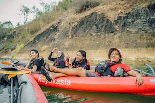 4 orang tersenyum duduk di perahu kayak dengan background pemandangan sungai dan batuan kapur