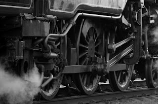 A black and white closeup of the wheels of a steam locomotive.