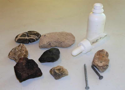 A picture of an eyedropper and steel nails with an assortment of rocks.
