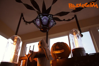 Night photo of glowing vintage-style Halloween lantern (The Horrid Decor #2 Pus & Bruise on Ghost Skin) by Bindlegrim hanging over a authentic vintage paper Jack O'Lantern pumpkin