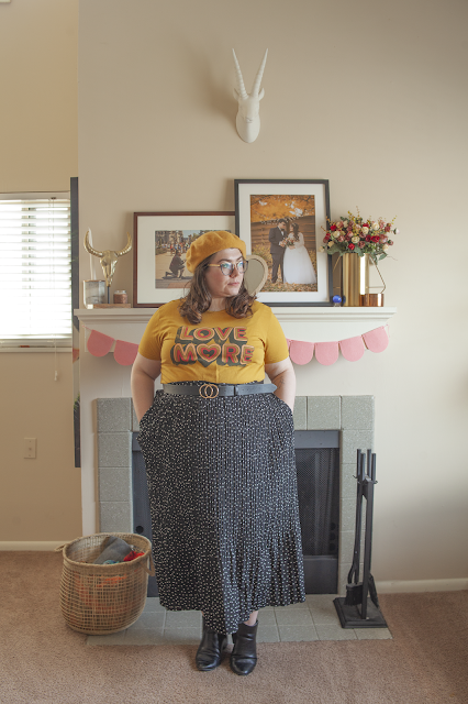 An outfit consisting of a yellow beret, yellow tee with a Love More print tucked into a black and white dotted maxi skirt and black chelsea boots.