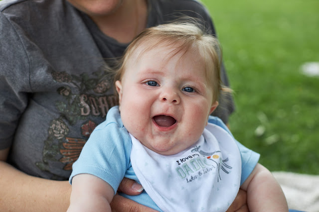 A smiley, open-mouthed, happy chubby baby sat on their mum's lap