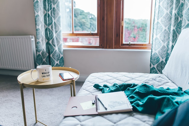 sofa with notebook, pen and blanket and side table with mug and phone