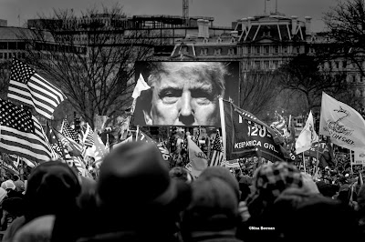 Black and white photo of President Trump on giant screen at a rally outside the White House.