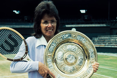 Billie Jean King (white woman with big brunette hair) holding a tennis racket and a big golden plate