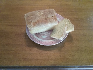 A loaf of home-made white bread on a pink transferware plate; two slices have been cut off and laid down next to the rest of the loaf.