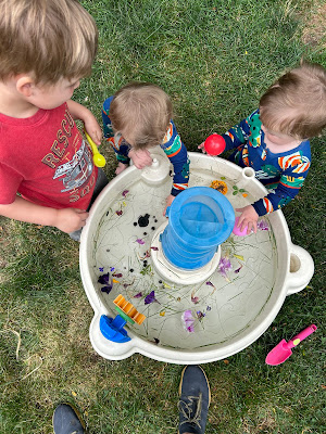 Three blonde toddlers playing outside in the grass at a water table