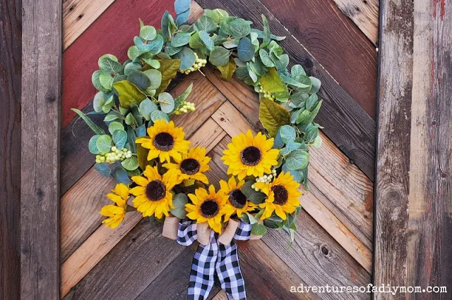 bright sunflower wreath easy diy tutorial finished and hanging on a wood fence.