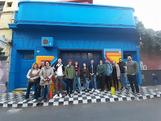 Treze pessoas estão em pé em frente a uma casa colorida e grafitada, em Palermo Soho, Buenos Aires. São estudantes da escola Expanish.
