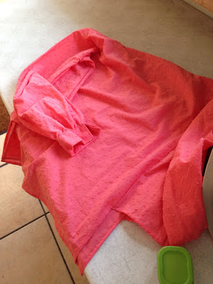 A salmon-pink blouse with long, gathered sleeves, laid out on a white counter.