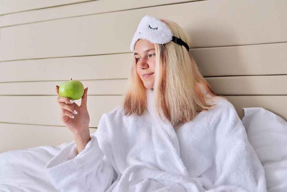 Joven que despierta en una cama con una manzana en la mano