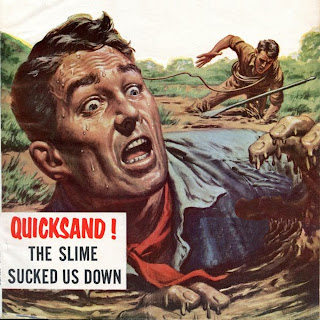 Close up of an anxious, sweating man sunk up to his shoulders in quicksand. Brown hair, blue eyes. He wears a blue work shirt with a red neckerchief. His left hand drips mud as he holds it up, as his right hand rests on the surface of the quicksand. In the background, a man in brown shirt and pants scrambles with a rope and boat oar, up to his knees in quicksand. A caption at lower left reads, "QUICKSAND! THE SLIME SUCKED US DOWN."