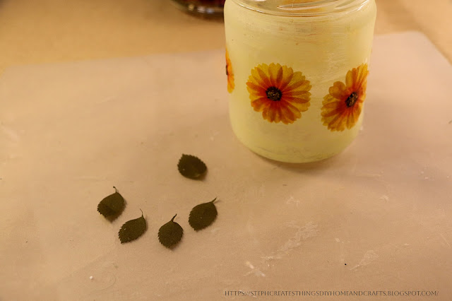 Glass jar with paper flowers and craft leaves nearby on a table