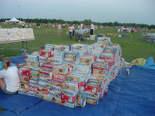 Boxes of Saltine Crackers mounded into a small hill on a blue tarp in the foreground and tables full of water bottles in the background