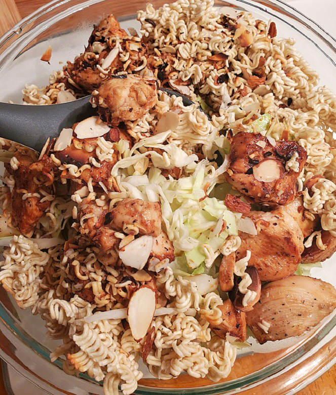 this is a large see through glass bowl filled with Asian salad which as chicken, cabbage slaw in a tangy dressing with toasted almonds