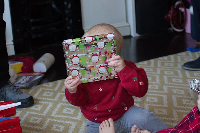 Baby Boy in Next Christmas jumper hiding behind a present