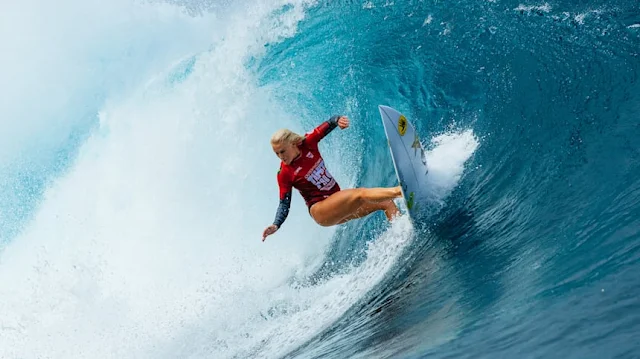 De vermelho, Tatiana Weston-Webb surfa em onda. Ela é uma mulher loira e branca
