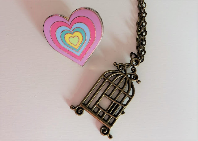 Multicoloured heart pin badge next to dark gold cage necklace