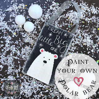 A dark hand painted plaque painted with a polar bear and snowflakes. The handwritten quote on the plaque says 'Dream Big little one' and is threaded with silver ribbon to hang on a door.   