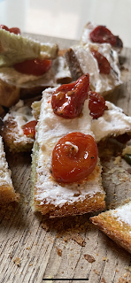 A close up of a pile of bread pieces, slavered with white cream cheese, with glistening cherry tomatoes haves on top.