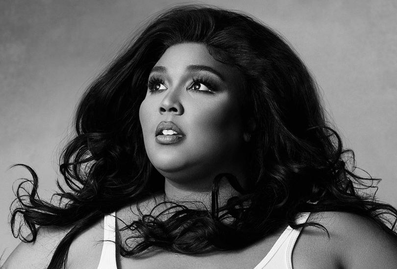 A black and white shot of Lizzo looking off to her right, wearing a white tank top, as her hair blows.