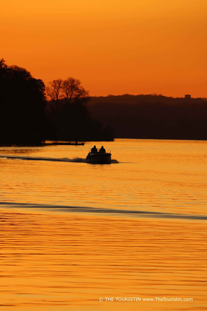The silhouette of a boat with two passengers at sunset, whereby the water, as well as the sky, is bathed in a deep orange colour.