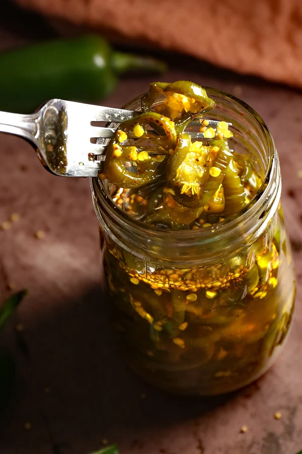 A captivating close-up of a jar filled with delicious cowboy candy. A fork is seen digging into the jar, lifting up succulent candied jalapenos. The vibrant colors and enticing textures of the jalapenos make for an irresistible treat, combining sweetness and heat in every bite.