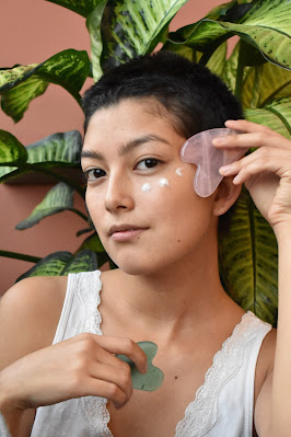 Mujer haciendo el gesto de masajearse crema sobre el rostro ayudándose de piedras semipreciosas