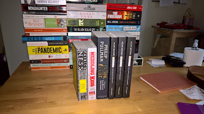 A collection of books on a kitchen table with a smaller collection on front, all for reading
