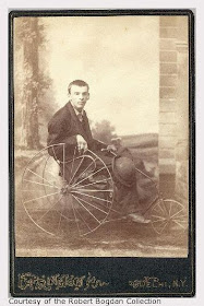 Vintage, sepia tone photo of a young man in an old-style wheelchair, wearing a suit and holding a cane and bowler hat