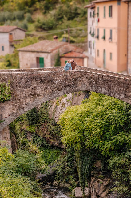 due innamorati si baciano sopra un ponticino romanico in un contesto fiabesco