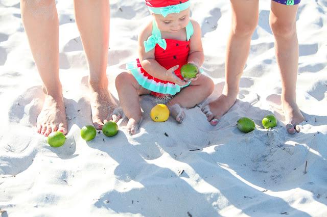 infant in watermelon bathing suit playing with limes
