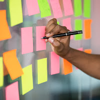 A hand writes plans on multi-colored post-it notes