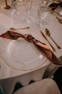 gold beaded charger with brown knot napkin fold and gold silverware