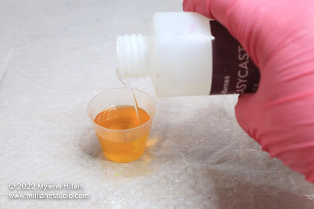 Gloved hand measuring resin into a medicine cup