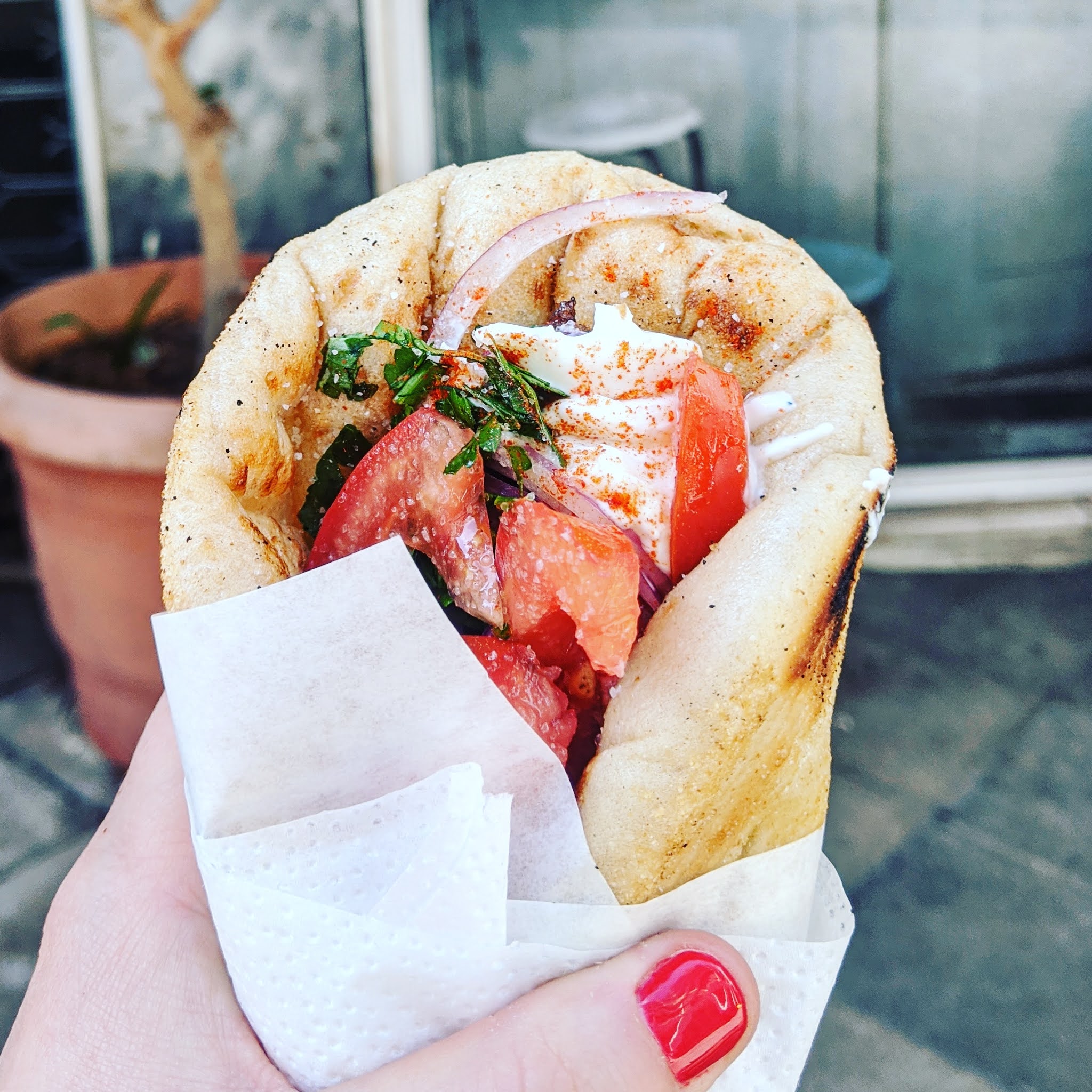 hand with painted nails holding a pork souvlaki outside kostas in greece athens