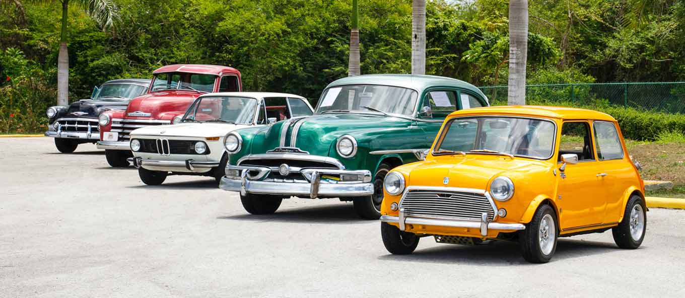 Wide photo taken of five beautiful classic cars that are parked in a line featuring a classic Mini in yellow and white BMW