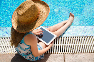 Niña con sombrero de paja, sentada a la orilla de la piscina, con una tablet.