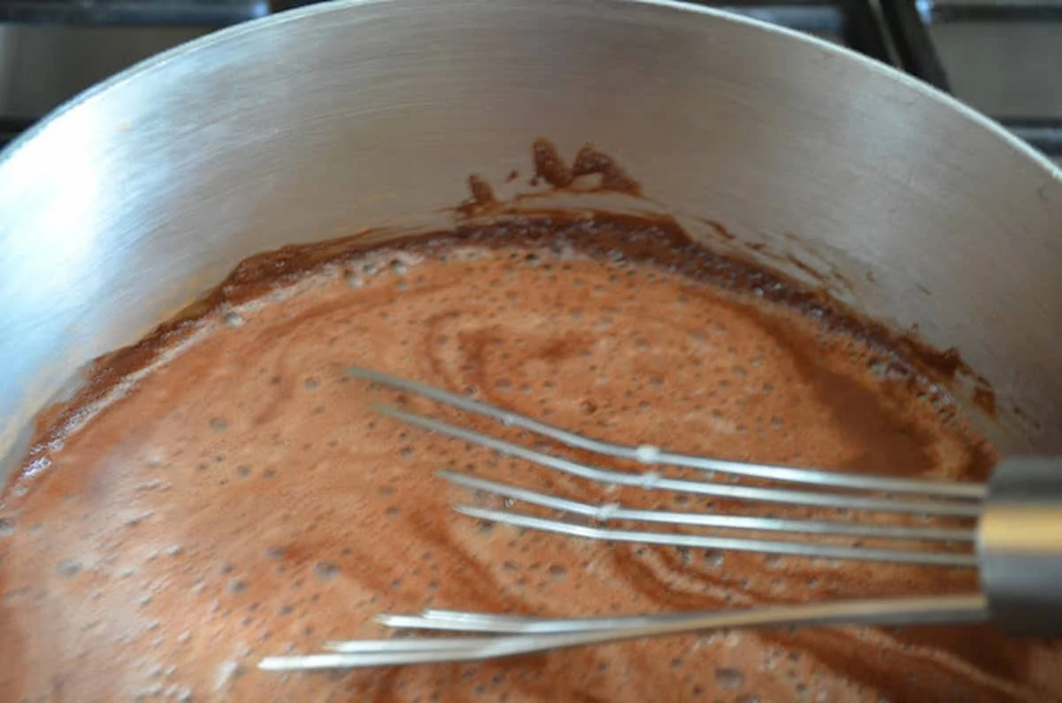 Milk and cream whisked into cocoa powder sugar mixture in a stainless steel pan.
