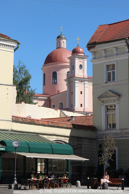 Small city square in Vilnius with the pastel coloured Orthodox Church of the Holy Spirit in the background.