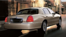 Rear 3/4 view of 2011 Lincoln Town Car driving on wet city street